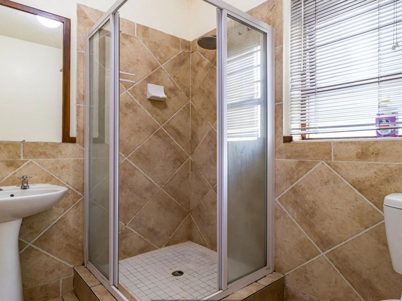 A functional bathroom featuring a pedestal basin, a glass-enclosed shower, and a toilet, finished with neutral-toned wall and floor tiles.