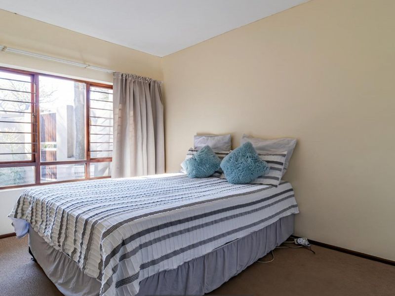 A functional bedroom featuring carpeted flooring and a large window with security bars, offering natural light and a neutral color palette.