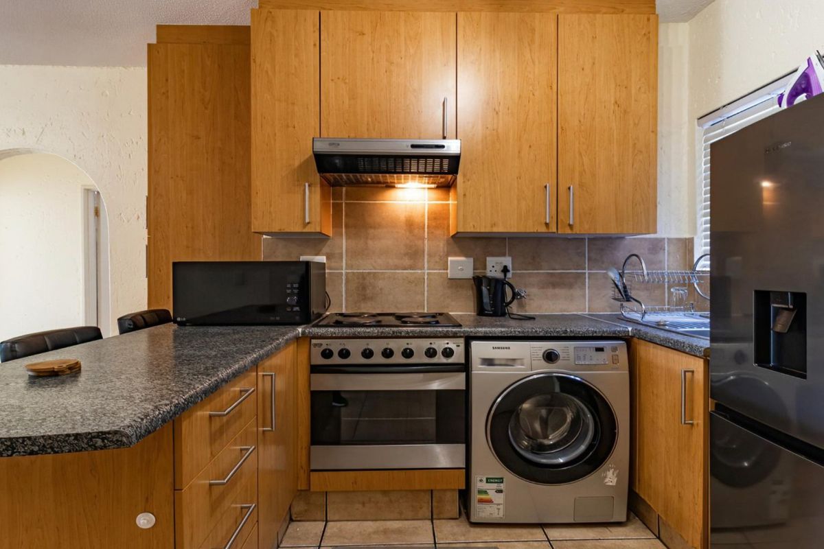 A functional kitchen featuring wooden cabinetry, granite countertops, a tiled backsplash, and integrated appliances including a gas hob, oven, and washing machine.