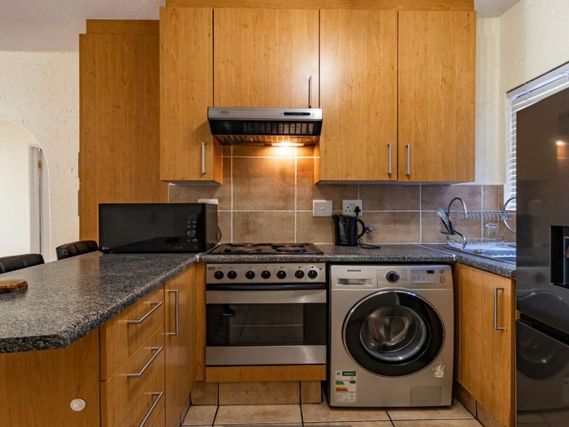A functional kitchen featuring wooden cabinetry, granite countertops, a tiled backsplash, and integrated appliances including a gas hob, oven, and washing machine.