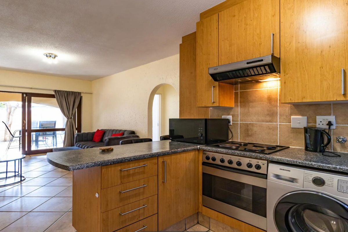 Open-plan kitchen featuring wooden cabinetry, granite countertops, and integrated appliances, flowing into a living area with access to an outdoor patio.