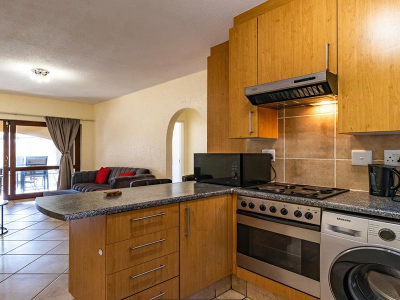Open-plan kitchen featuring wooden cabinetry, granite countertops, and integrated appliances, flowing into a living area with access to an outdoor patio.