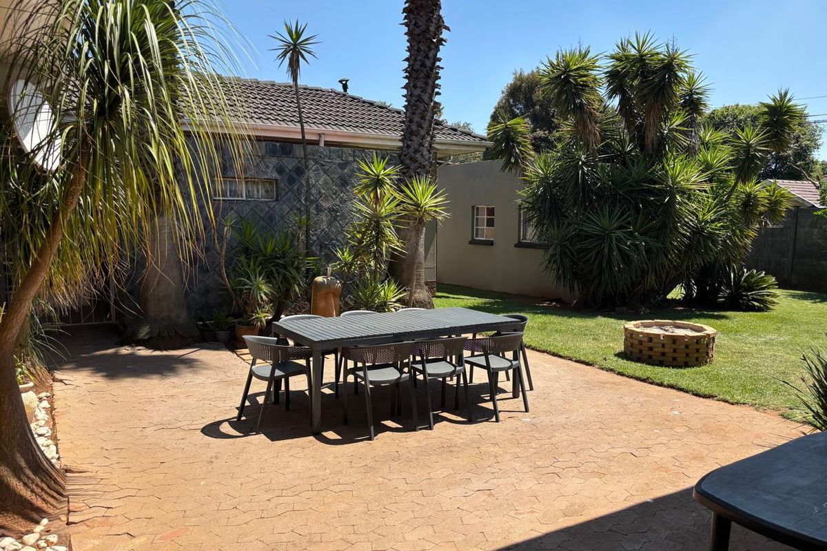 A spacious rear garden featuring a paved patio area, a built-in brick fire pit, and established landscaping with stone-clad exterior walls.