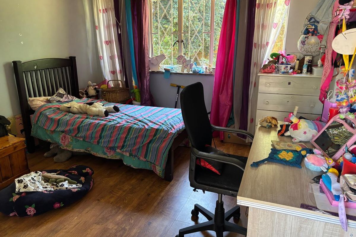 A functional bedroom featuring laminate flooring and a window fitted with security burglar bars.