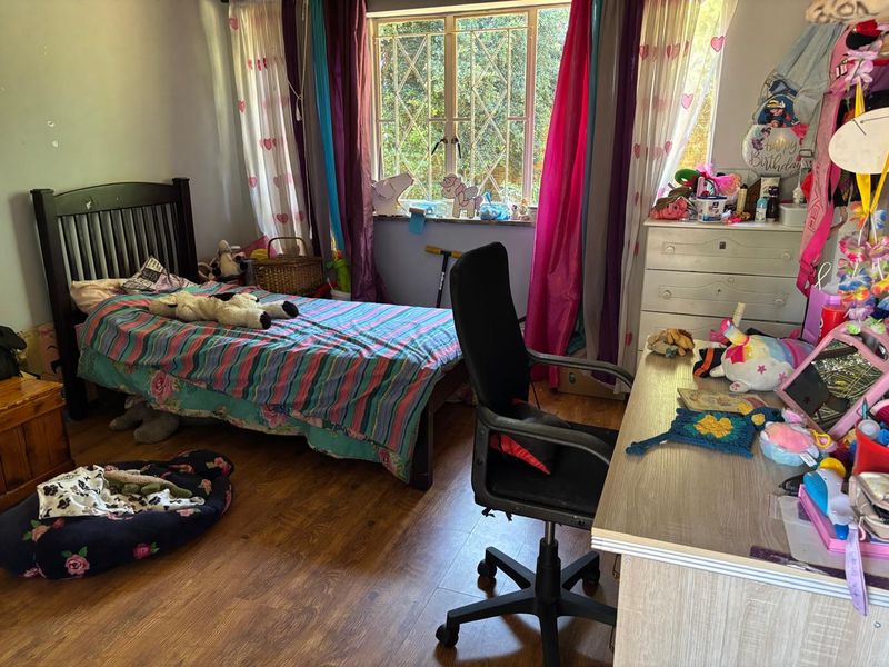 A functional bedroom featuring laminate flooring and a window fitted with security burglar bars.
