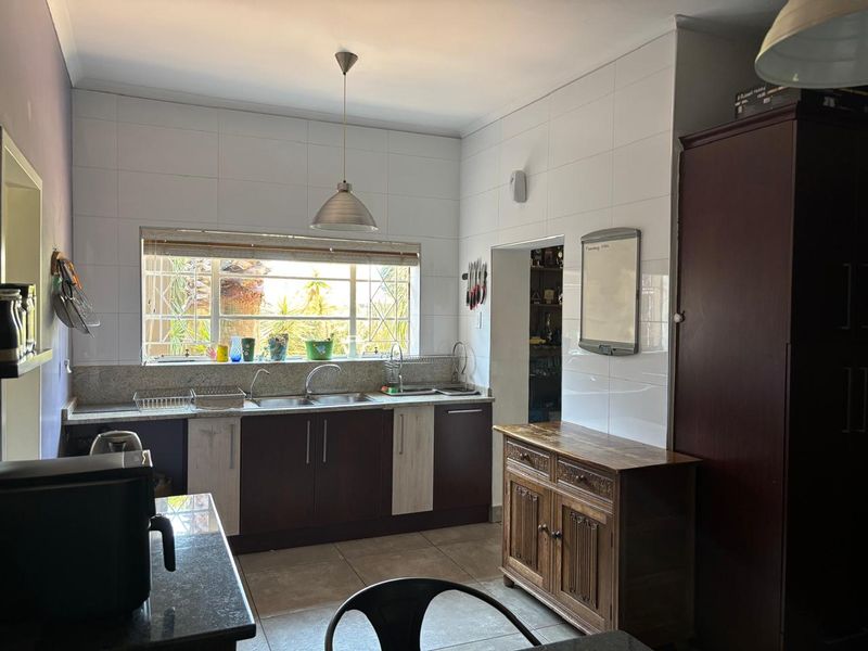 A functional kitchen featuring granite countertops, a double basin sink, tiled splashback, and tiled flooring with natural light from a window.