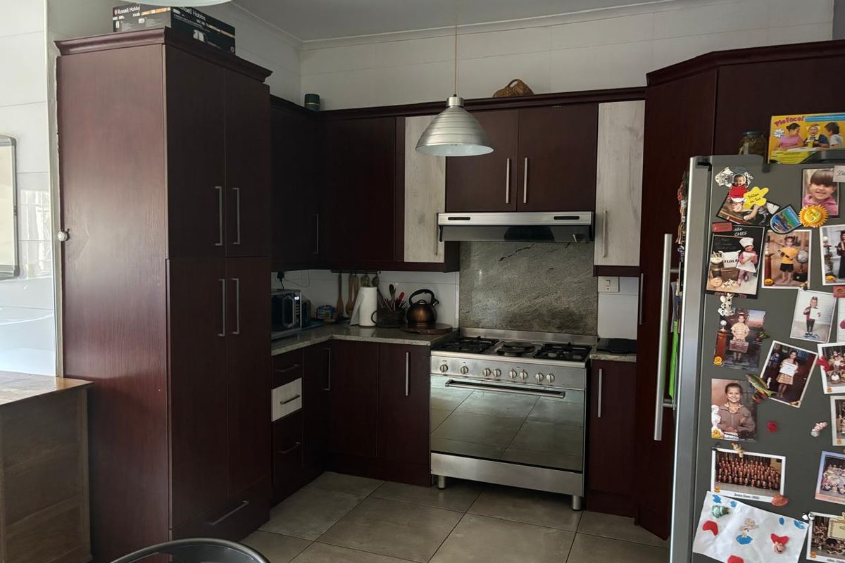 A functional kitchen featuring dark wood cabinetry, a stainless steel gas stove with extractor fan, stone splashback, and neutral floor tiles.