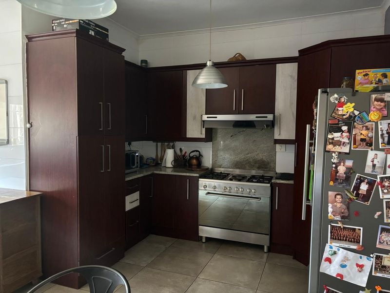A functional kitchen featuring dark wood cabinetry, a stainless steel gas stove with extractor fan, stone splashback, and neutral floor tiles.