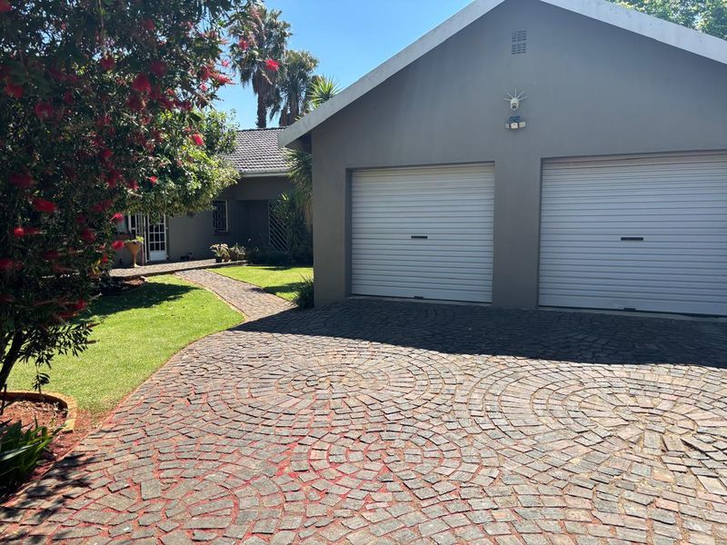 Front exterior view featuring a double garage with roller shutter doors, a decorative cobbled driveway, and a paved walkway leading to the entrance.