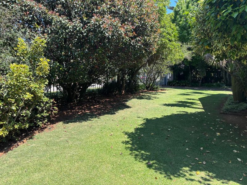 A well-maintained garden area featuring a lush green lawn, mature trees, and established perimeter fencing.