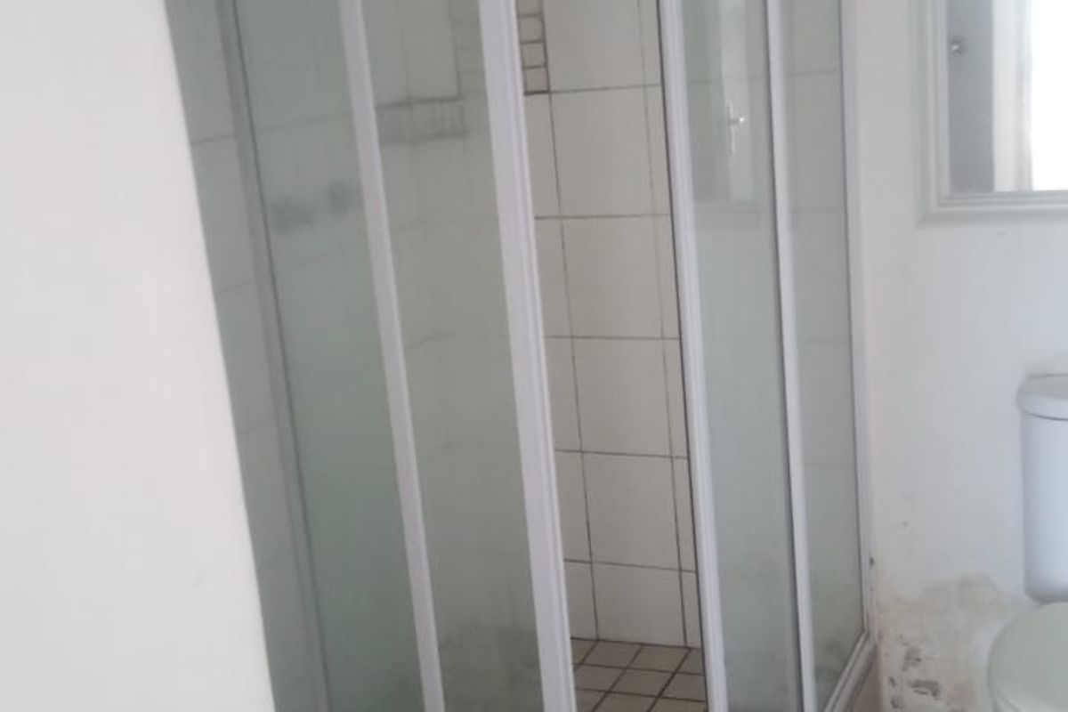 A compact bathroom featuring a corner shower enclosure, tiled flooring, and wall tiles, currently showing signs of wear and water damage.