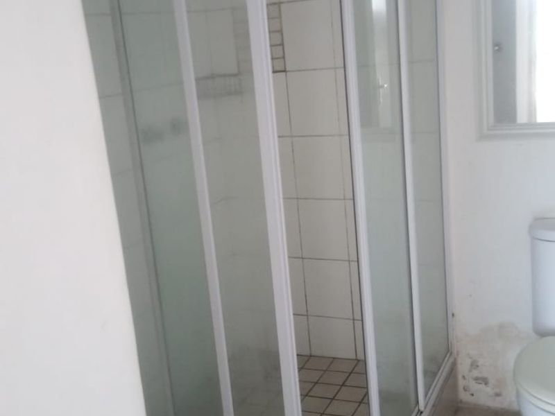 A compact bathroom featuring a corner shower enclosure, tiled flooring, and wall tiles, currently showing signs of wear and water damage.