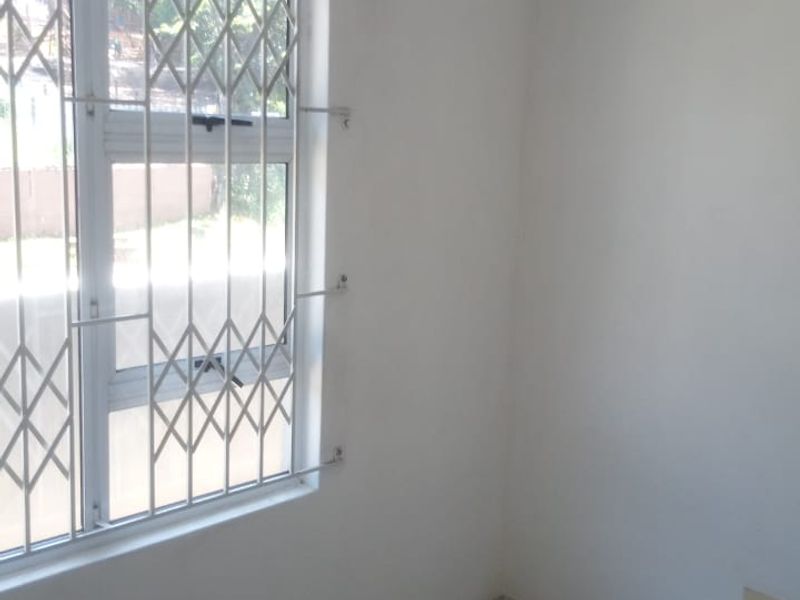 A clean, empty bedroom featuring tiled flooring, neutral walls, and a window fitted with a security gate.