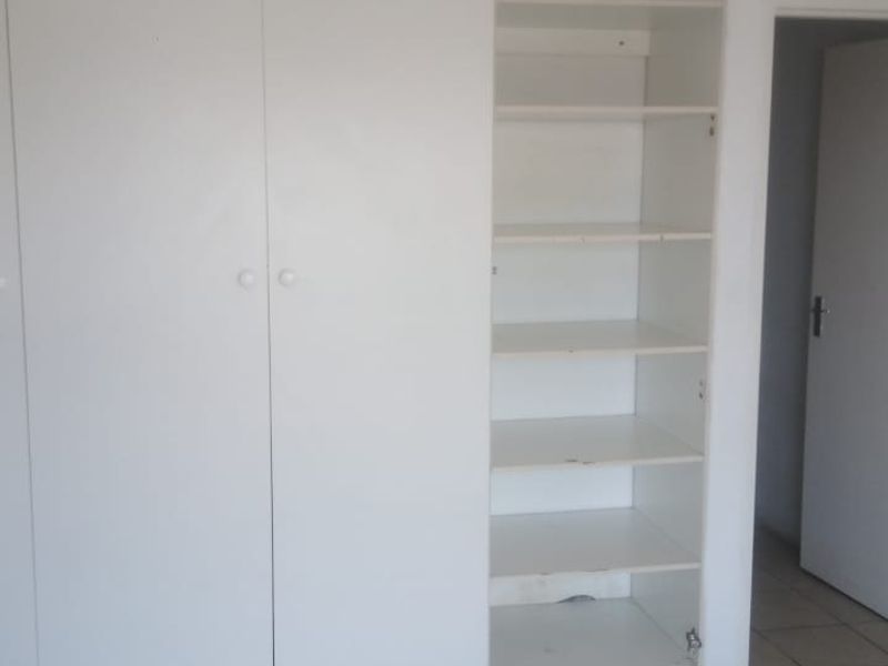 A bedroom featuring white built-in cupboards with open shelving and neutral tiled flooring.