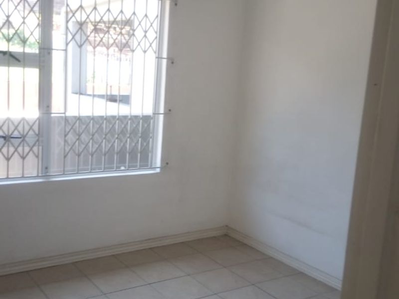 An empty bedroom featuring tiled flooring and security bars on the window, providing a blank canvas for personalization.