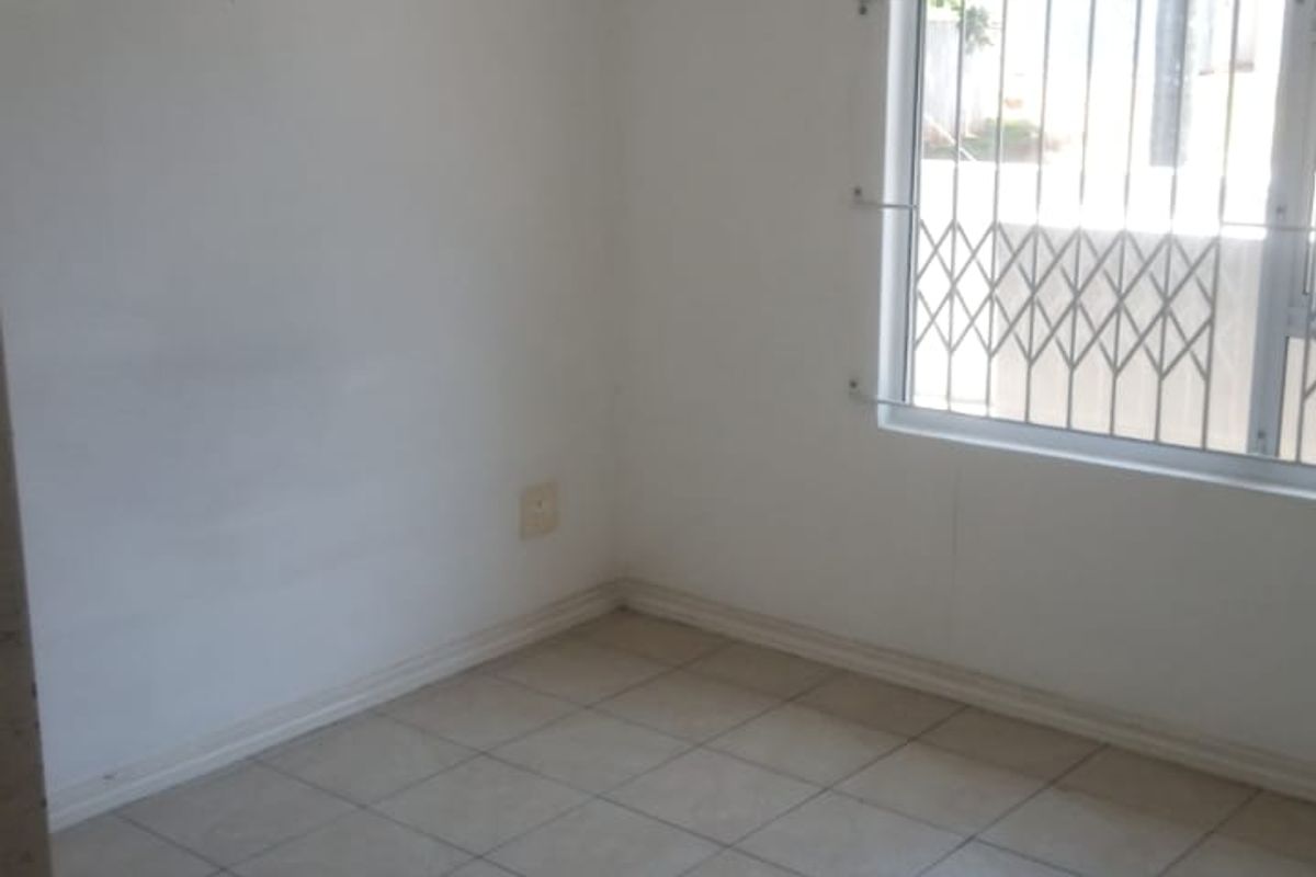 An empty bedroom featuring tiled flooring and a window fitted with a security gate.