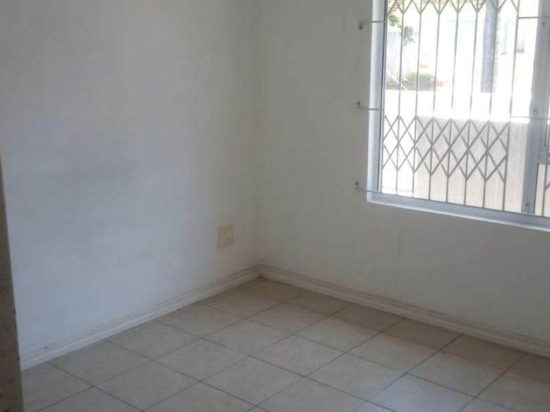 An empty bedroom featuring tiled flooring and a window fitted with a security gate.