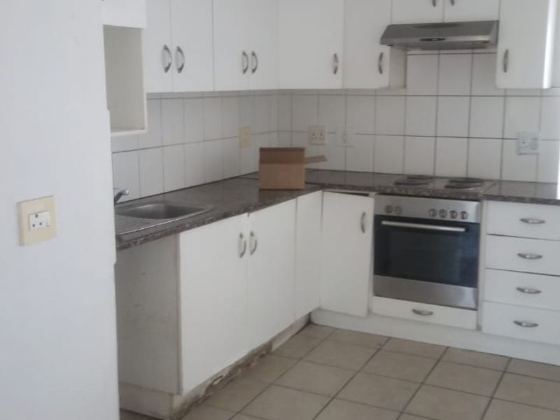 A functional kitchen featuring white cabinetry, built-in oven, hob, and extractor fan, with tiled flooring and backsplash. Requires maintenance to address visible water damage.