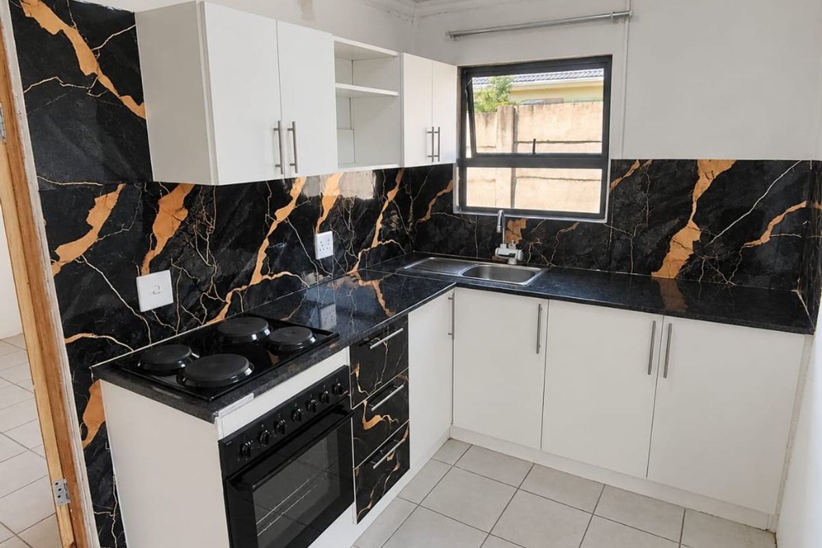 Compact kitchen featuring white cabinetry, black marble-look splashbacks, built-in oven, electric hob, and stainless steel sink with tiled flooring.