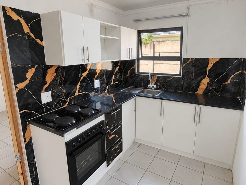 Compact kitchen featuring white cabinetry, black marble-look splashbacks, built-in oven, electric hob, and stainless steel sink with tiled flooring.