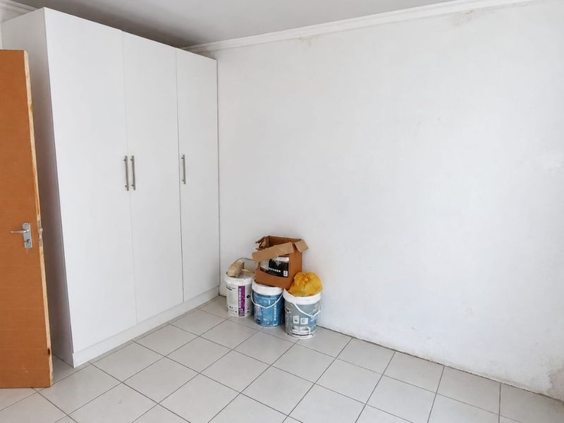 A simple, empty bedroom featuring neutral tiled flooring and a built-in white wardrobe, offering a clean canvas for personalization.