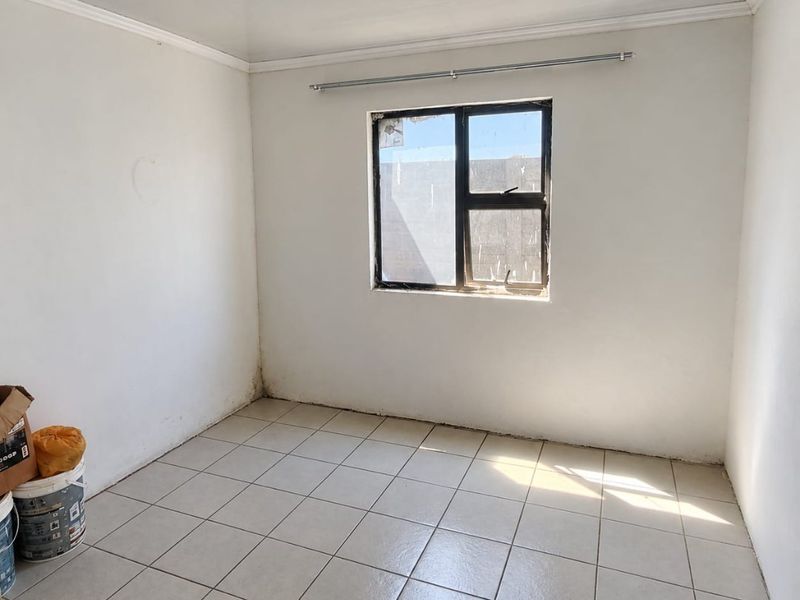 An empty bedroom featuring tiled flooring, a coved ceiling, and an aluminium window frame, ready for personalization.