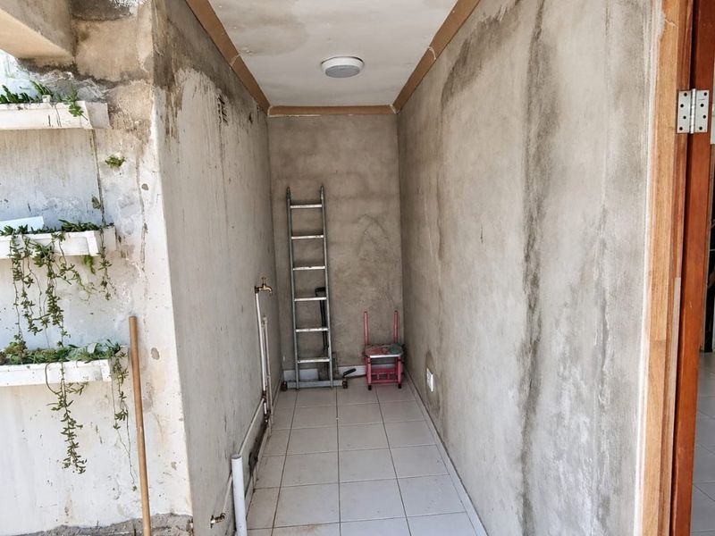 A utility space featuring tiled flooring and unfinished concrete walls with plumbing connections, requiring cosmetic finishing and maintenance to address wall and ceiling condition.