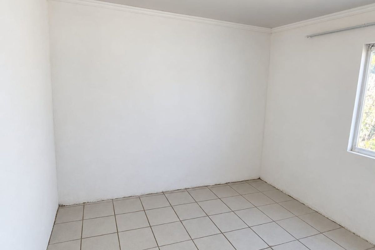 A clean, empty bedroom featuring neutral tiled flooring, white walls, and ceiling cornicing, ready for personalization.