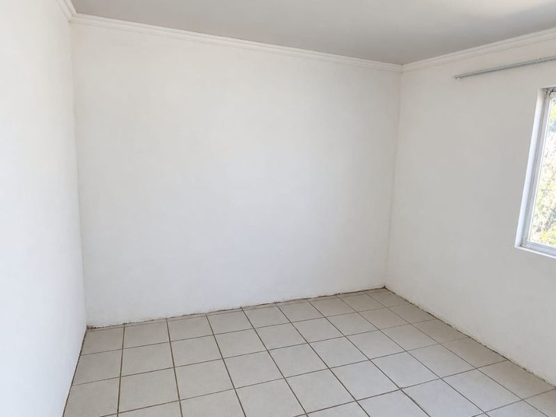 A clean, empty bedroom featuring neutral tiled flooring, white walls, and ceiling cornicing, ready for personalization.