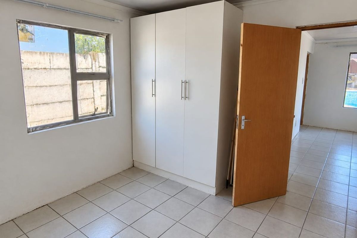 A bright, empty bedroom featuring neutral tiled flooring, a built-in white wardrobe, and a large window providing natural light.