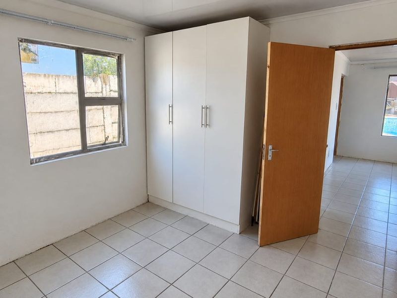 A bright, empty bedroom featuring neutral tiled flooring, a built-in white wardrobe, and a large window providing natural light.
