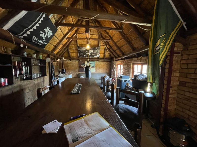 A rustic bar area featuring a traditional thatched roof with exposed timber rafters and exposed brick walls, creating a cozy, character-filled entertainment space.