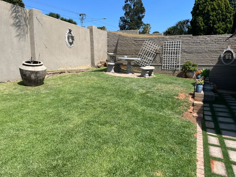 A private rear garden featuring a lawn area, perimeter boundary walls, and paved pathways.