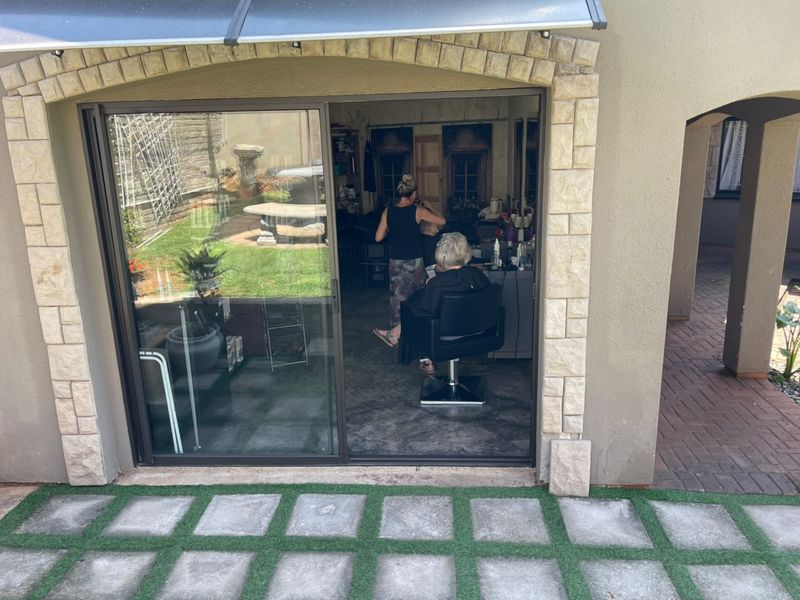 A covered patio area featuring stone cladding, a sliding glass door entrance, and a paved outdoor space with artificial grass accents.