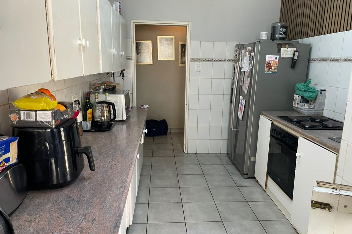 A functional kitchen featuring tiled flooring, laminate countertops, built-in oven, and electric hob, with overhead cabinetry providing ample storage space.