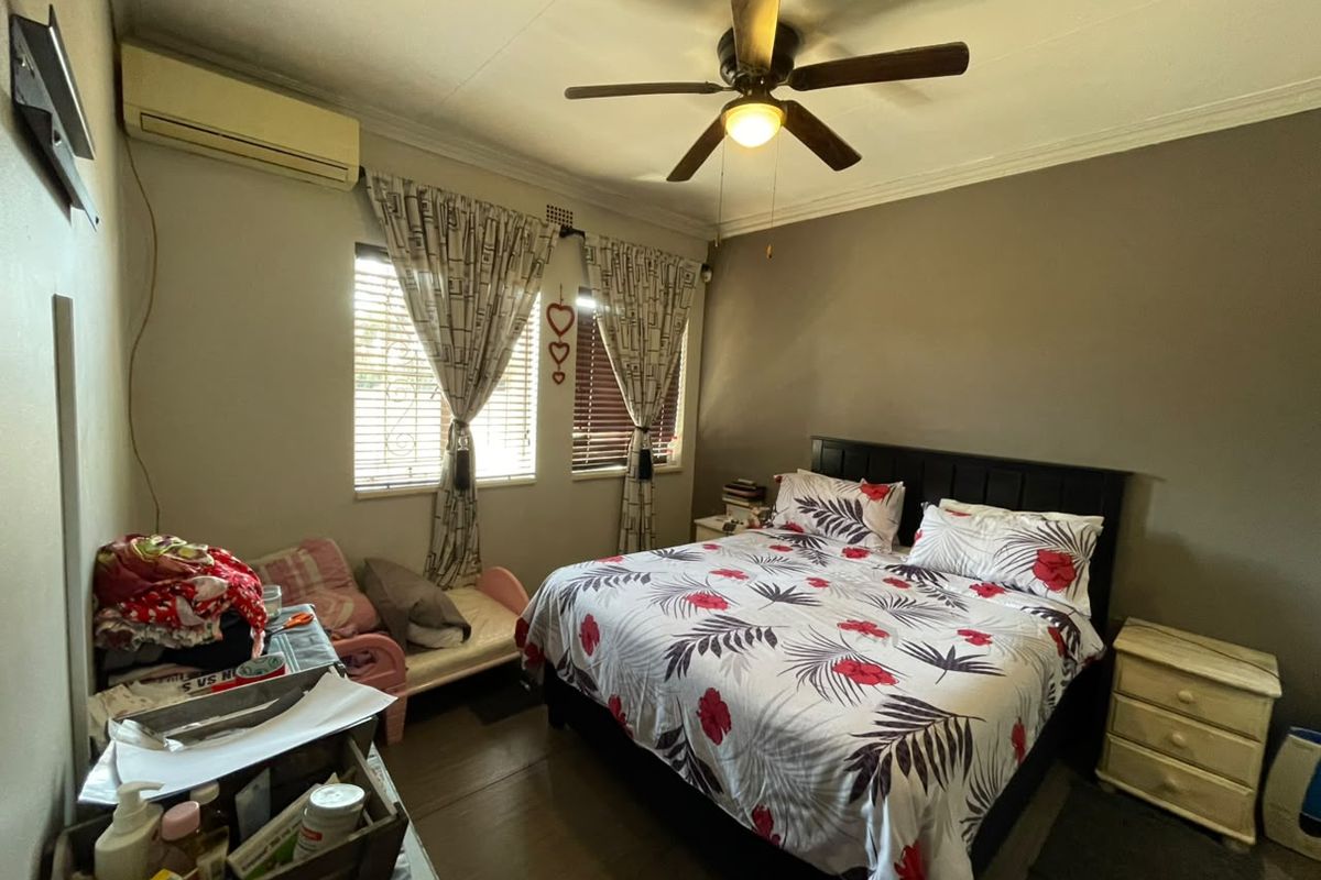 A functional bedroom featuring a ceiling fan, split-system air conditioning unit, and security bars on the windows.