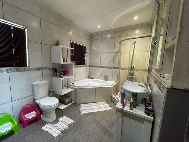 A functional bathroom featuring a corner bathtub, separate glass shower enclosure, pedestal basin, and neutral wall tiling with decorative mosaic accents.