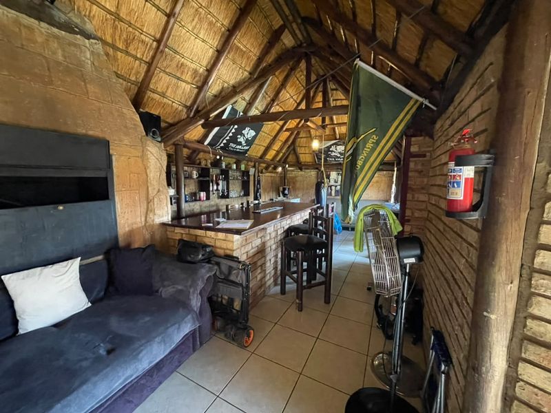 Rustic bar area featuring a high thatched roof with exposed timber trusses, built-in brick bar counter, and tiled flooring.