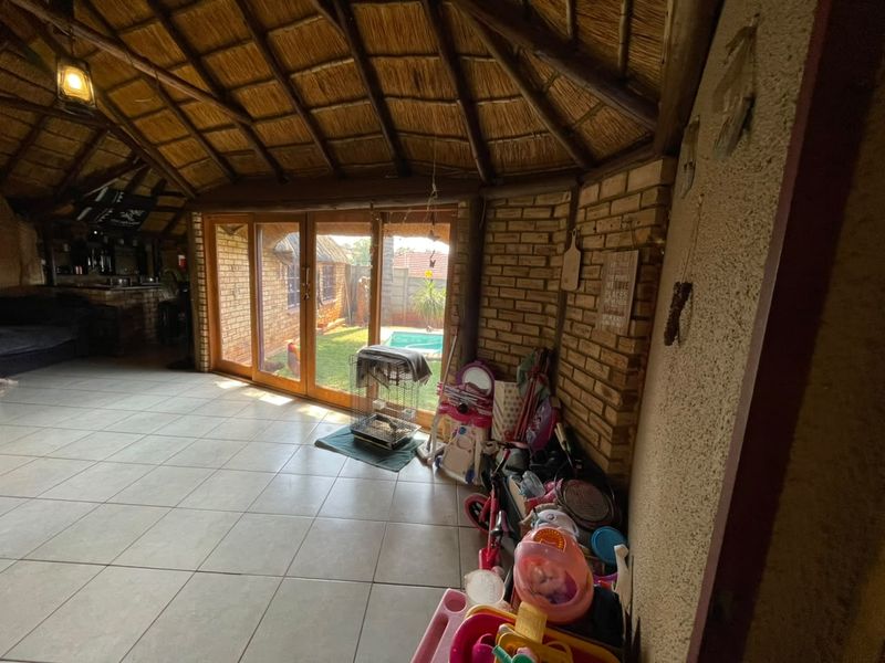 Spacious covered patio featuring a traditional thatched roof, exposed brickwork, and large sliding doors opening onto the garden and pool area.