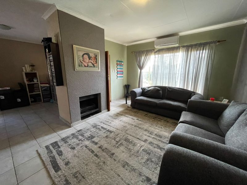 A comfortable living room featuring a built-in fireplace, tiled flooring, and a wall-mounted air conditioning unit.