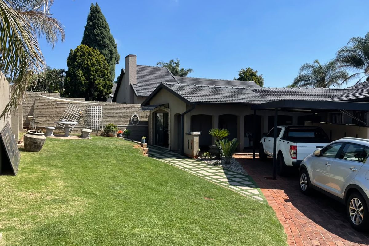 Rear exterior view featuring a well-maintained lawn, brick driveway, carport, and paved walkway leading to the house entrance.