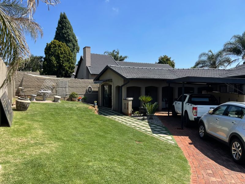 Rear exterior view featuring a well-maintained lawn, brick driveway, carport, and paved walkway leading to the house entrance.