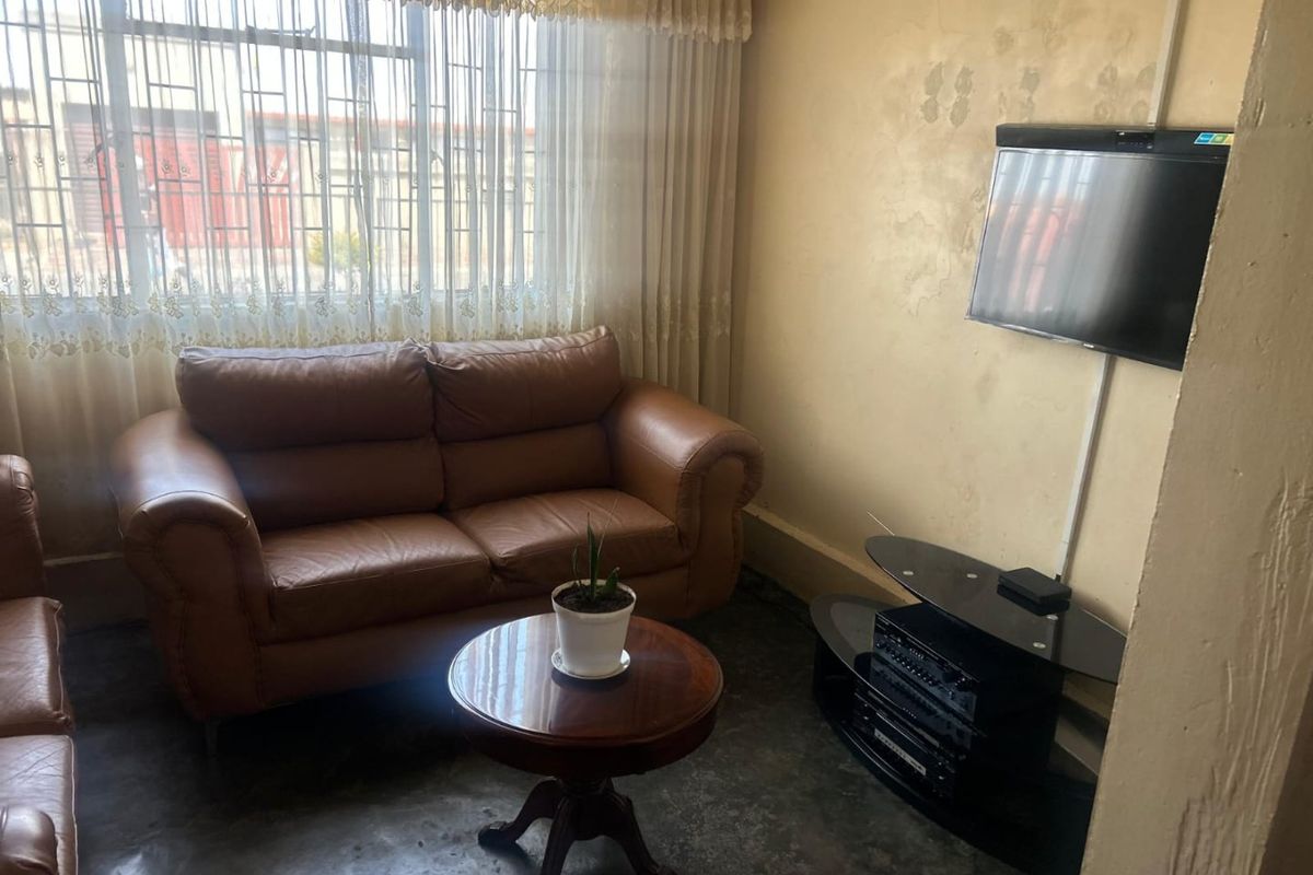 A living room area featuring a window with security bars and visible wall surface deterioration requiring maintenance and cosmetic updates.