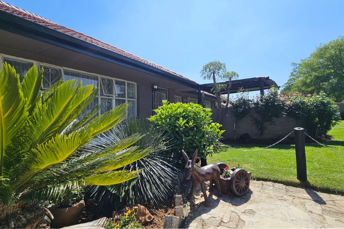 A view of the rear exterior featuring a paved patio area, well-maintained lawn, and a boundary wall with established garden landscaping.