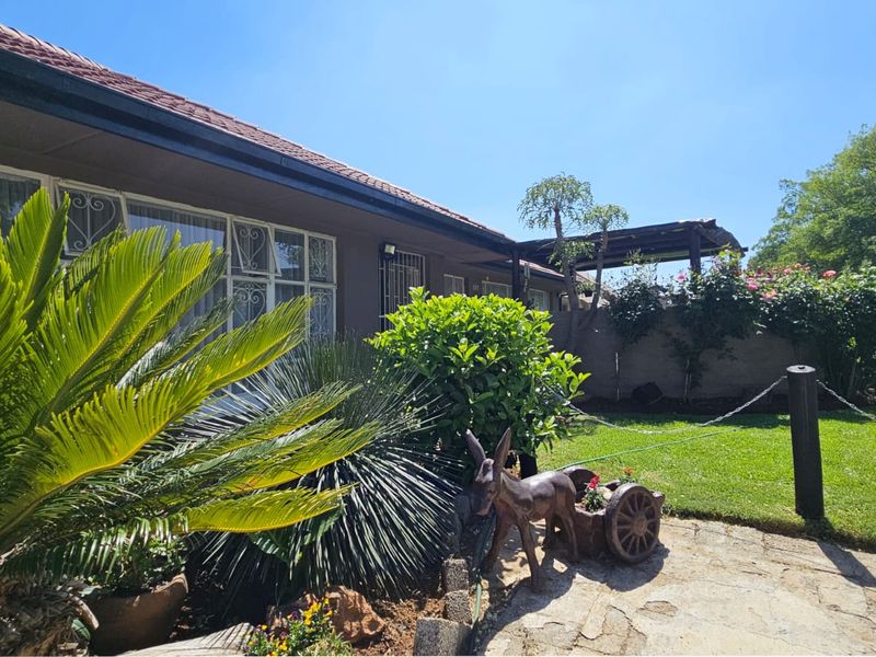 A view of the rear exterior featuring a paved patio area, well-maintained lawn, and a boundary wall with established garden landscaping.