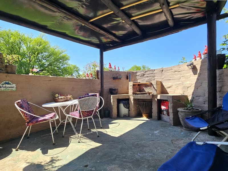 Outdoor patio area featuring a covered timber pergola, built-in masonry braai, and concrete flooring, providing a functional space for outdoor entertaining.