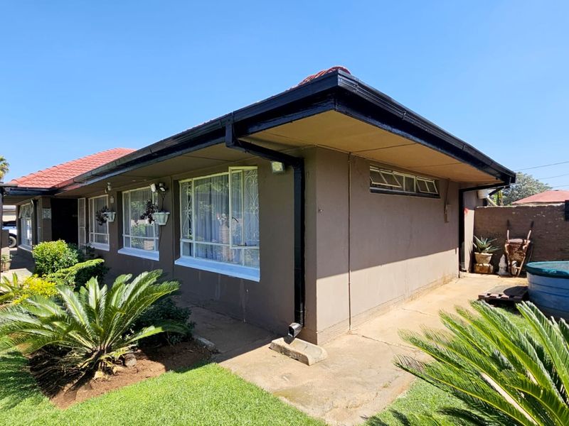 Rear exterior view of the house featuring a tiled roof, concrete pathways, and established garden area with boundary walling.