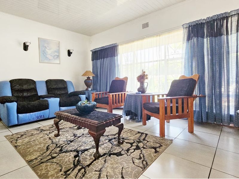 A bright living room featuring tiled flooring, a large window with natural light, and classic wall-mounted light fixtures.