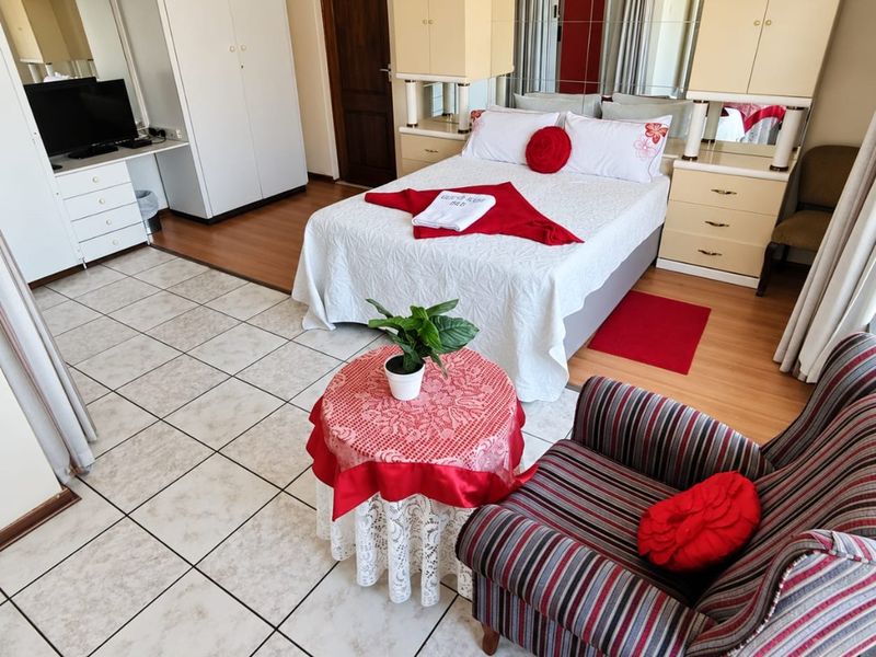 A bedroom featuring built-in cupboards, a built-in headboard with integrated mirrors, and a combination of tiled and laminate flooring.