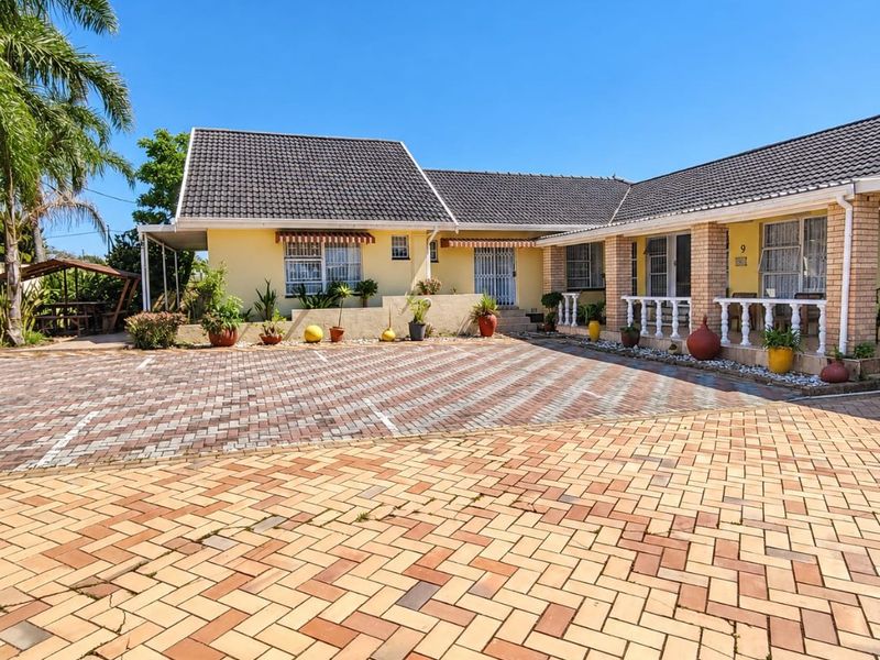 Front elevation of a single-story residence featuring a large paved driveway, tiled roof, and a covered porch area with decorative balustrades.